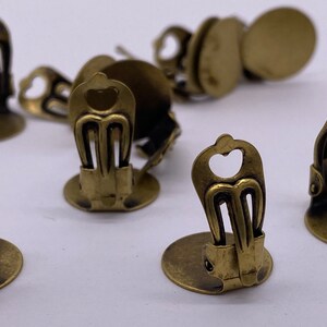 May include: A set of 10 antique brass earring clips. The clips are round with a heart-shaped cutout and a decorative design. The clips are designed to be used with earring findings.