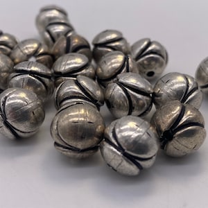 May include: A pile of silver metal beads with a flower-like design. The beads are round and have a textured surface.