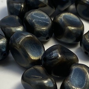 Könnte beinhalten: Eine Gruppe dunkelblauer und goldfarbener, irisierender Glasperlen. Die Perlen sind glatt und haben eine leicht unregelmäßige Form.