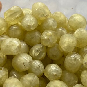 May include: A close-up of a pile of translucent, pale yellow, faceted beads. The beads are smooth and have a slightly iridescent sheen.