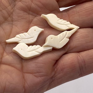 May include: Four white ceramic bird figurines, each with a detailed design, are displayed in a hand. The birds are all facing the same direction, with their wings spread out.