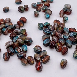 May include: Assortment of iridescent glass beads in shades of brown, blue, and green. The beads are oval shaped and have a shimmery finish.