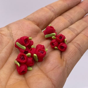 May include: A collection of small, red rose flower embellishments with green leaves. The roses are made of polymer clay and are perfect for adding a touch of elegance to crafts and projects.