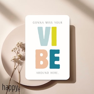 Könnte beinhalten: Eine weiße rechteckige Karte mit den Worten "GONNA MISS YOUR VIBE AROUND HERE" in einer farbenfrohen, verspielten Schriftart. Das Wort "VIBE" ist in Blau, Gelb, Pfirsich und Türkis gehalten. Die Karte befindet sich auf einem neutralen Hintergrund mit einem Zweig weißer Blumen.