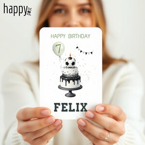 May include: A birthday card featuring a two-tiered cake with a soccer ball on top, a balloon with the number 7, and the name "FELIX". The words "HAPPY BIRTHDAY" are at the top of the card. The card has a black and white color scheme.
