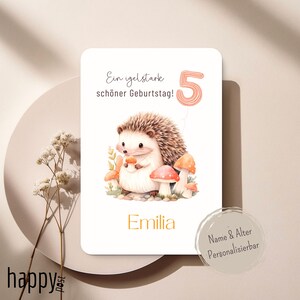 Peut inclure: Carte d'anniversaire avec une illustration à l'aquarelle d'un hérisson tenant un champignon, entouré d'autres champignons. Le chiffre 5 est affiché comme un ballon. La carte comprend le nom "Emilia" et le texte "Ein igelstarke schöner Geburtstag!"