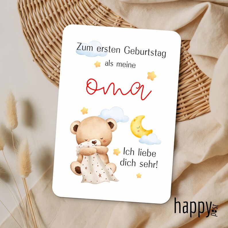 May include: A white card with German text and a cute illustration. The text reads "Zum ersten Geburtstag als meine Oma Ich liebe dich sehr!" with a red "Oma" in the middle. The illustration features a teddy bear, clouds, stars, and a crescent moon.