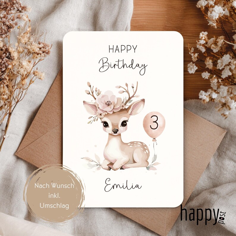 May include: A birthday card with a watercolor illustration of a fawn wearing a floral crown and holding a balloon with the number 3. The card reads "Happy Birthday" and "Emilia". Includes a brown envelope.