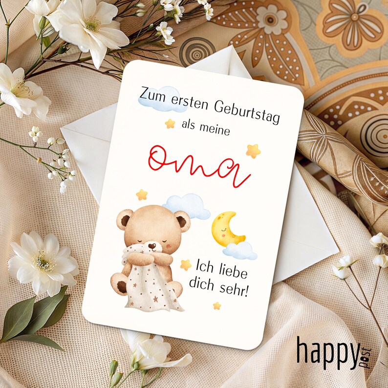 May include: A greeting card with the text "Zum ersten Geburtstag als meine Oma" in black and red. The card features a teddy bear holding a blanket, a crescent moon, and stars. The word "happy post" is in the bottom right corner.
