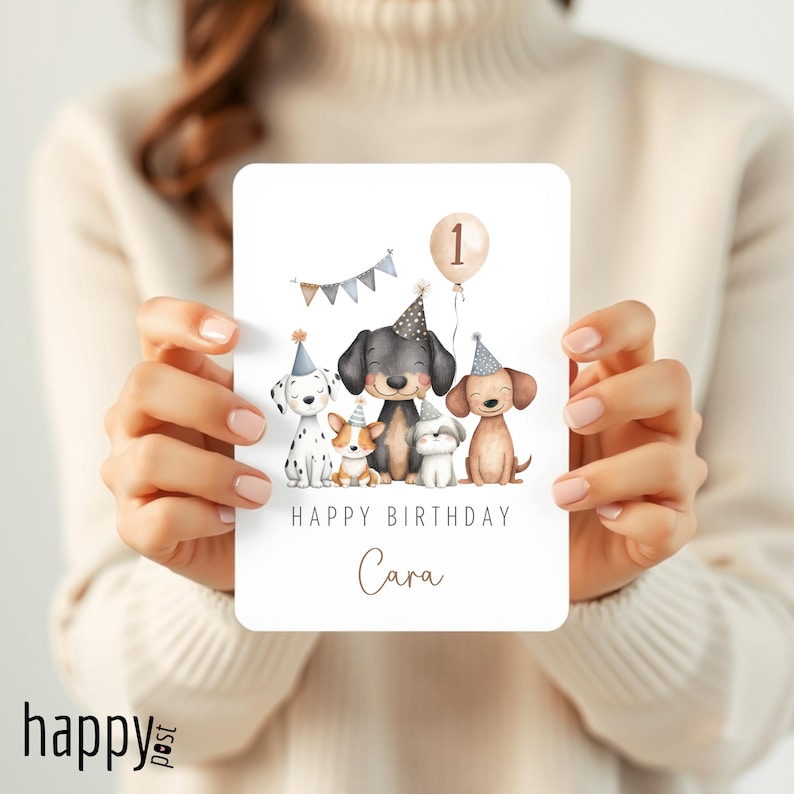 May include: A birthday card featuring a watercolor illustration of five dogs wearing party hats. A balloon with the number 1 floats above the dogs. The card reads "Happy Birthday Cara."