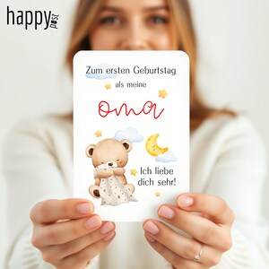 May include: A white card with German text and a teddy bear illustration. The card reads "Zum ersten Geburtstag als meine Oma" and "Ich liebe dich sehr!" A teddy bear is hugging a blanket with stars, and a yellow moon is also shown.