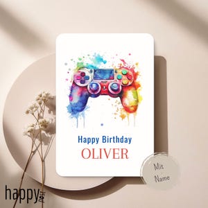 Könnte beinhalten: Weiße Geburtstagskarte mit einem Aquarellbild eines bunten Gamecontrollers. Der Text "Happy Birthday OLIVER" steht darunter. Ein kleiner Aufkleber mit "Mit Name" befindet sich unten rechts.
