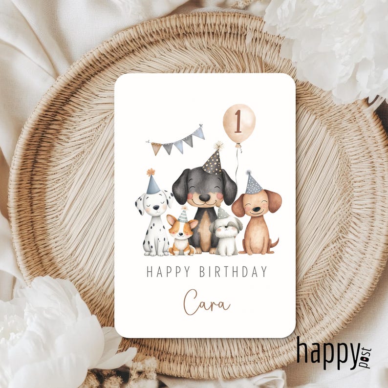 May include: A rectangular birthday card featuring a watercolor illustration of six cartoon dogs wearing party hats. The card reads "Happy Birthday Cara" with a balloon and banner. The card is on a woven surface.