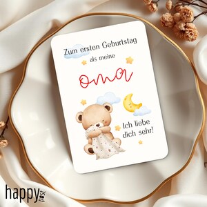 May include: A greeting card with a teddy bear illustration, clouds, and a crescent moon. The card has text in German that says "Zum ersten Geburtstag als meine Oma. Ich liebe dich sehr!" The card is on a white plate.
