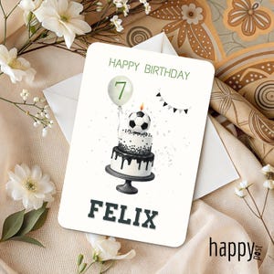 May include: A birthday card with a soccer ball cake design. The card says "Happy Birthday" and "Felix" in green and black lettering. A green balloon with the number 7 is also featured.