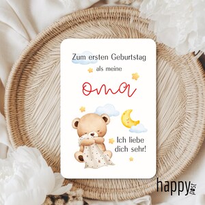 May include: A rectangular card with text and illustrations. The text reads "Zum ersten Geburtstag als meine Oma" and "Ich liebe dich sehr!". The illustrations include a teddy bear, clouds, a crescent moon, and stars. The card has a light background.