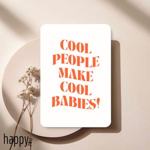 Może przedstawiać: Biała prostokątna karta z pomarańczowym napisem "COOL PEOPLE MAKE COOL BABIES!" na neutralnym tle. Karta umieszczona jest na jasnym talerzu z gałązką suszonych kwiatów.
