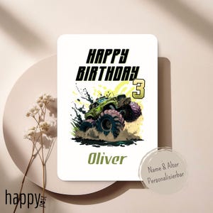May include: A white birthday card with a green monster truck graphic. The card reads "HAPPY BIRTHDAY 3" in black and yellow, with the name "Oliver" in green. The card is on a beige surface.