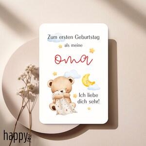 May include: A white card with German text and a watercolor illustration of a teddy bear, moon, and stars. The text reads "Zum ersten Geburtstag als meine Oma. Ich liebe dich sehr!" in red and black.