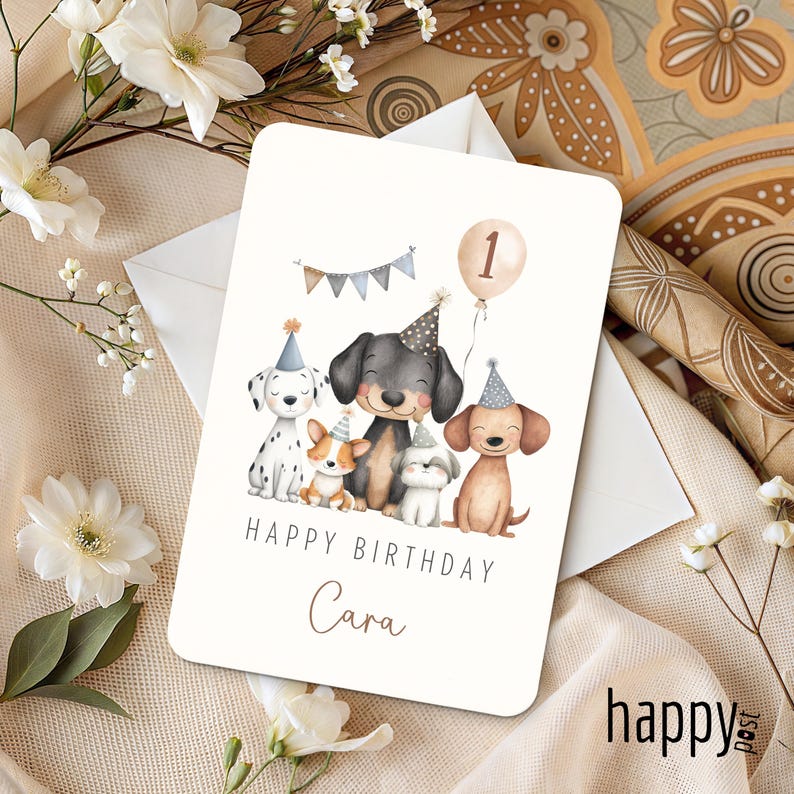 May include: A birthday card featuring illustrations of five dogs wearing party hats. The card reads "Happy Birthday Cara" with a balloon displaying the number one. The background is a soft beige with floral accents.