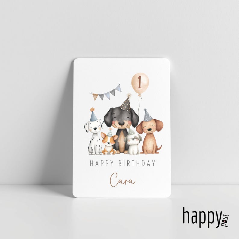 May include: A white birthday card featuring watercolor illustrations of five dogs wearing party hats. A balloon with the number 1 floats above them. The card reads "Happy Birthday Cara."