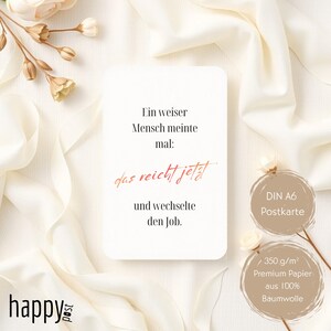 May include: A white postcard with the text "Ein weiser Mensch meinte mal: das reicht jetzt und wechselte den Job." in black and red. The postcard is surrounded by white fabric and flowers. The postcard is a DIN A6 size.