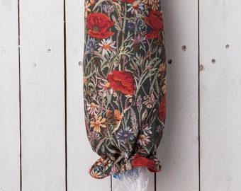 Pode incluir: Um dispensador de sacolas de compras de tecido com interior vermelho e um padrão floral com papoulas vermelhas, margaridas brancas e outras flores silvestres em um fundo escuro. A sacola está pendurada em um gancho de metal.