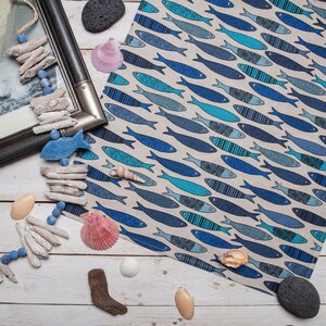 May include: A blue and white kitchen towel with a pattern of fish. The towel is lying on a white wooden surface with driftwood, seashells, and stones.