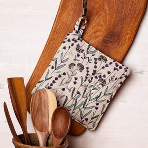 Peut inclure: Un ensemble de cuillères en bois dans un vase en céramique brun avec un porte-pot en tissu à motif floral suspendu à une planche à découper en bois.