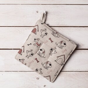 Könnte beinhalten: Ein beiger Topflappen mit einem Muster aus braunen Hunden und Knochen. Der Topflappen hat eine Schlaufe zum Aufhängen.