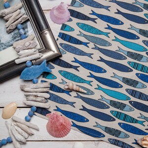 May include: A white background with a blue and white fabric with a pattern of blue fish. There are seashells, driftwood, and beads scattered around the fabric.