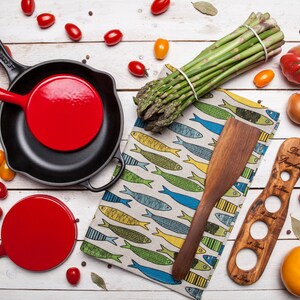 May include: A set of two red cast iron skillets with black handles, a wooden spatula, a wooden olive oil dispenser, a bunch of asparagus, and various vegetables on a white wooden surface.