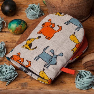 Puede incluir: Un guante de horno gris con un patrón de perro colorido. El guante tiene un lazo de colgar rojo y está hecho de una tela suave y texturizada.