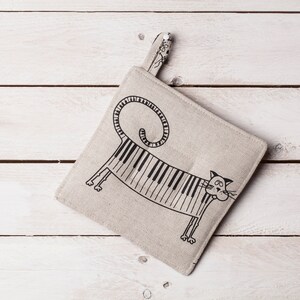 May include: A beige linen pot holder with a black and white illustration of a cat with a piano key pattern on its body.