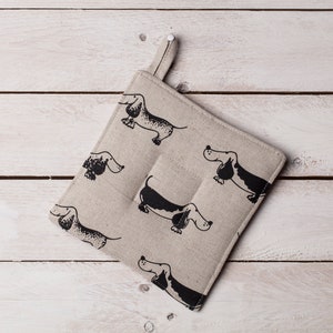 May include: A beige linen pot holder with a black and white dachshund print. The pot holder has a loop for hanging.