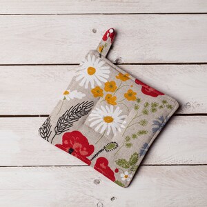 Può includere: Un sottopentola floreale con uno sfondo beige chiaro e un motivo di papaveri rossi, margherite bianche, fiori gialli e foglie verdi. Il sottopentola ha un anello per appenderlo.