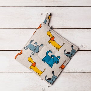 Può includere: Un sottopentola in cotone bianco con un motivo di cani colorati. I cani sono blu, gialli e arancioni. Il sottopentola ha un anello per appenderlo.
