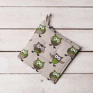 Può includere: Un sottopentola beige con un motivo di gufi verdi. Il sottopentola è realizzato in un tessuto morbido e trapuntato.