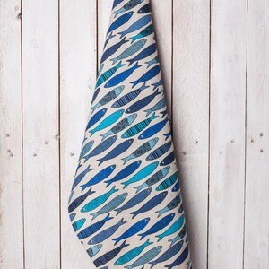 May include: A blue and white kitchen towel with a pattern of fish. The towel is hanging on a white wooden wall.