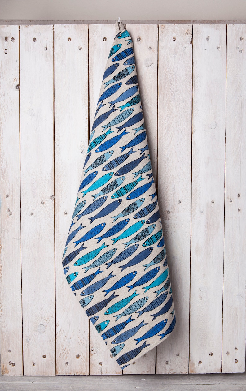 May include: A blue and white kitchen towel with a pattern of fish. The towel is hanging on a white wooden wall.