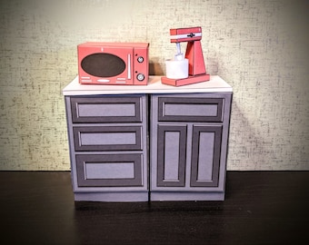 May include: A red microwave and a red stand mixer are on top of two gray cabinets with drawers. The cabinets are on a black surface.