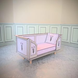 May include: A miniature, light purple sofa with a matching pillow. The sofa has a decorative floral design and is made of paper. The sofa is on small wooden legs and is set against a light-colored wall.