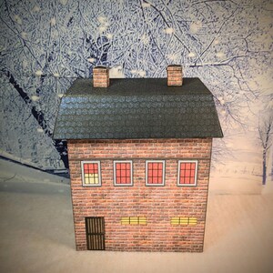 May include: A small, brick building with a gray roof and two chimneys. The building has four windows with red frames and two windows with yellow frames. The building has a black door with a metal grate.