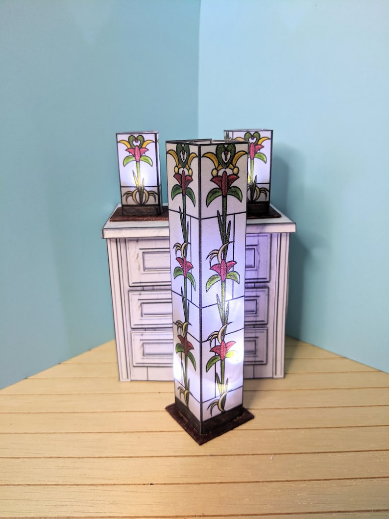 May include: Four decorative lamps with stained glass panels featuring a floral design. The lamps are made of paper and have a white background with red, yellow, and green flowers. The lamps are lit and casting a warm glow.