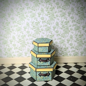 Puede incluir: Tres cajas hexagonales apiladas con un diseño de patrón azul y amarillo. Las cajas tienen asas marrones y están sobre un suelo de baldosas blancas y negras.