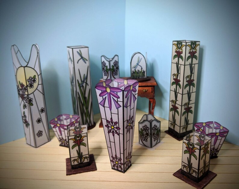 May include: A collection of eight stained glass lamps with floral and dragonfly designs. The lamps are in various shapes and sizes, and they are all made of clear glass with colorful accents. The lamps are arranged on a wooden surface.