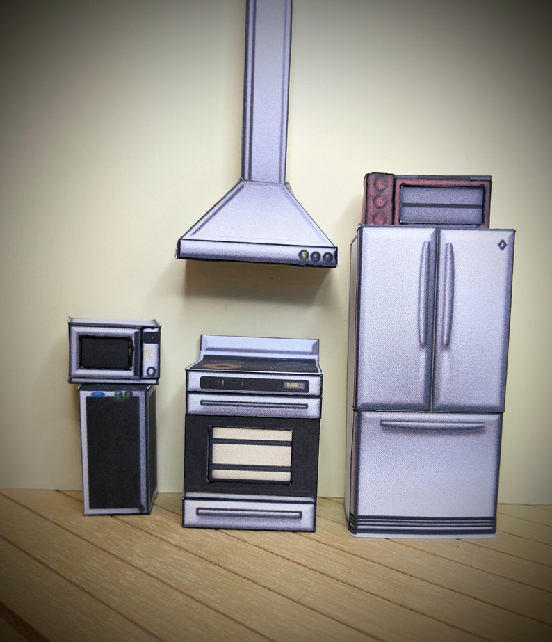 Pode incluir: Um conjunto de cozinha em miniatura com um refrigerador, forno e forno de micro-ondas de a&ccedil;o inoxid&aacute;vel. O conjunto tamb&eacute;m inclui um exaustor de a&ccedil;o inoxid&aacute;vel.