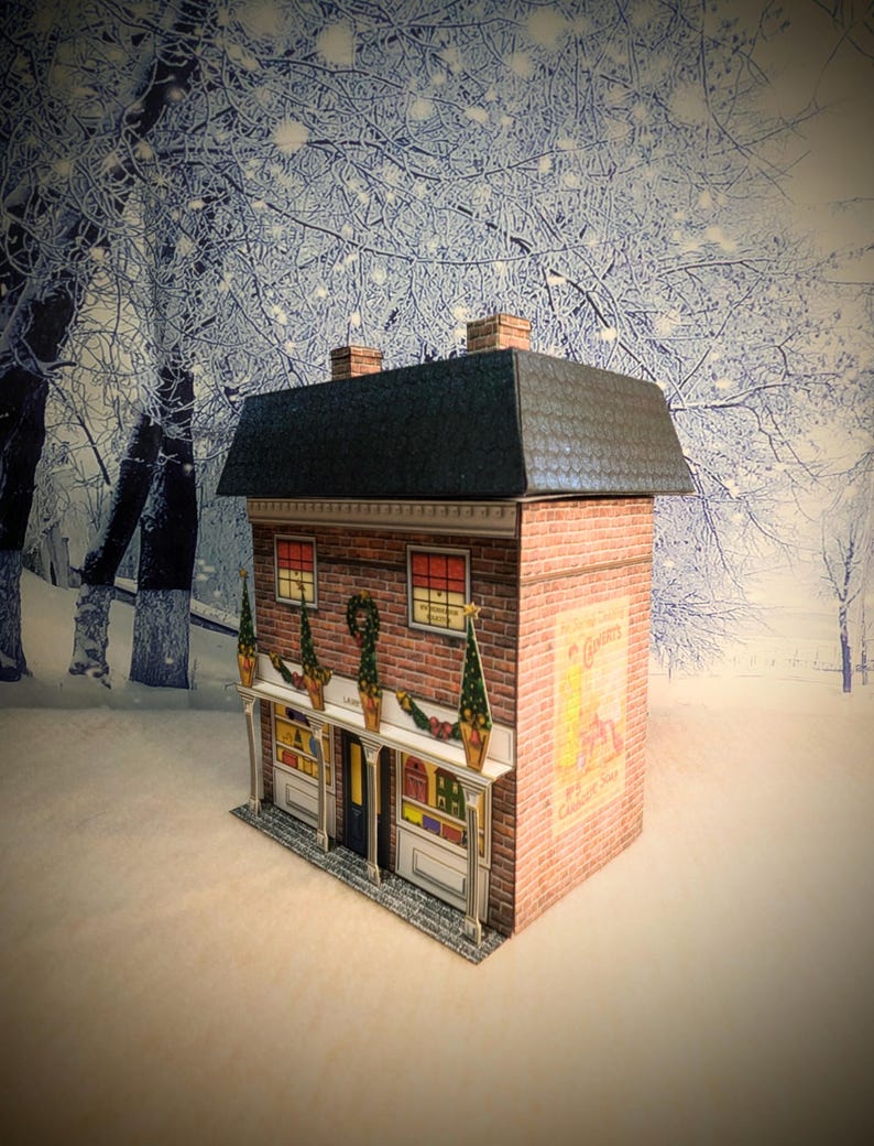 May include: A paper model of a brick building with a black roof and a sign that says "C. Gomery & Son, Wine & Spirit Stores". The building is decorated with Christmas lights and greenery.