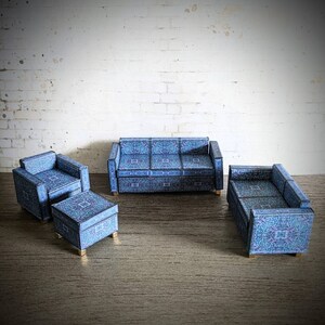 May include: A blue patterned living room set with a sofa, two armchairs, and a matching ottoman. The furniture is arranged on a wood floor in front of a white brick wall.