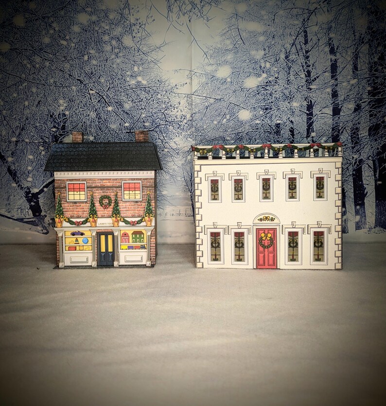 May include: Two paper model Christmas houses, one with a red door and a wreath, the other with a blue door and a sign that says "Candy Shop".